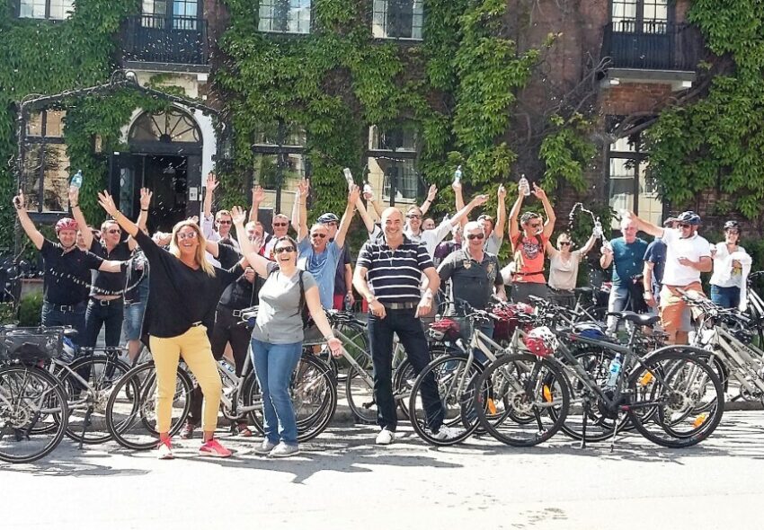 A large group of people with bikes pose happily in front of a building